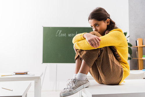 upset and bullied schoolgirl sitting alone in classroom