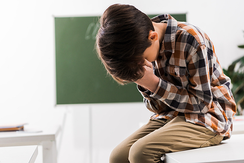 bullied schoolboy covering face while crying in classroom
