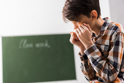bullied and depressed schoolboy covering face in classroom