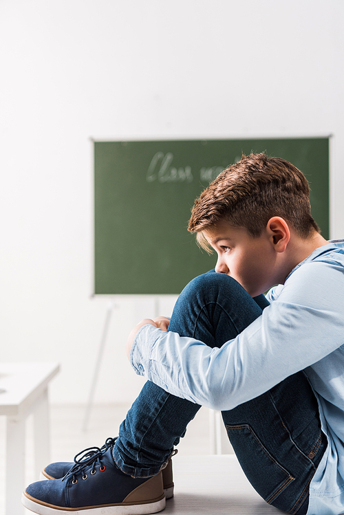 bullied schoolboy sitting on table in classroom