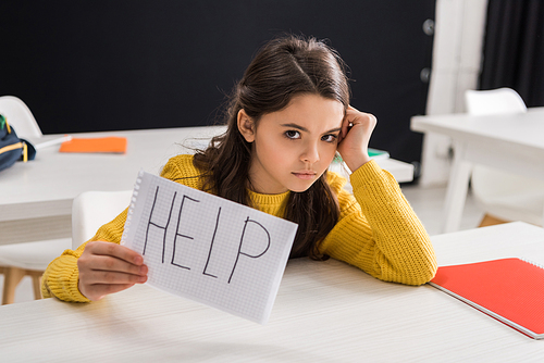 upset schoolgirl holding paper with help lettering, bullying concept