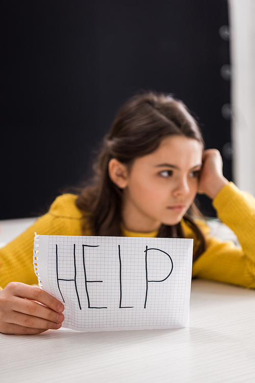 selective focus of paper with help lettering in hand of upset schoolgirl, bullying concept