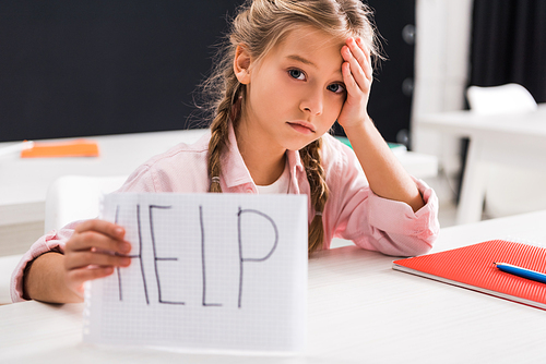 selective focus of sad schoolgirl holding paper with help lettering, bullying concept