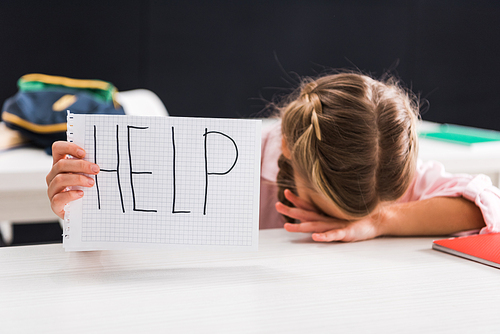 upset schoolgirl holding paper with help lettering, bullying concept