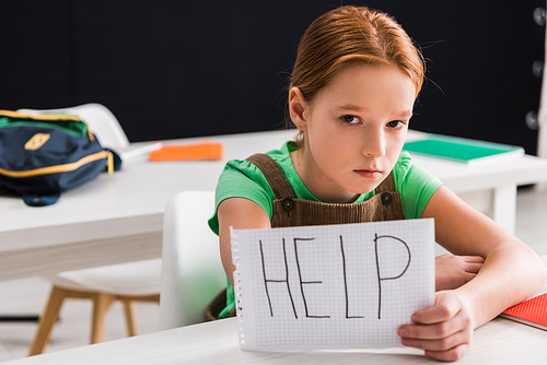 selective focus of depressed schoolkid holding paper with help lettering, bullying concept