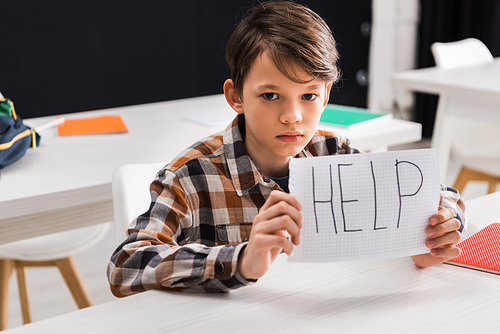 selective focus of upset schoolboy holding paper with help lettering, bullying concept