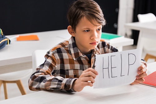 selective focus of sad schoolboy holding paper with help lettering, bullying concept