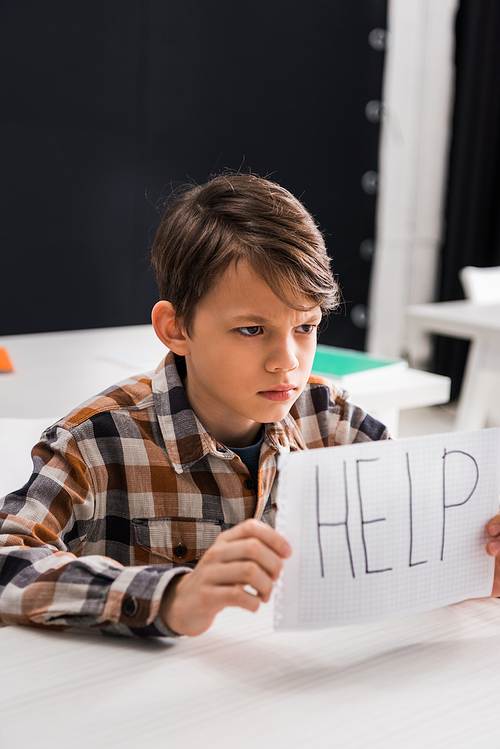 selective focus of depressed schoolboy holding paper with help lettering, bullying concept