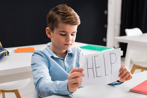 selective focus of depressed schoolchild holding paper with help lettering, bullying concept