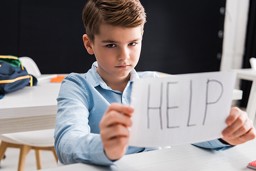 selective focus of depressed schoolkid holding paper with help lettering, bullying concept