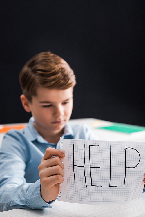 selective focus of frustrated schoolkid holding paper with help lettering, bullying concept