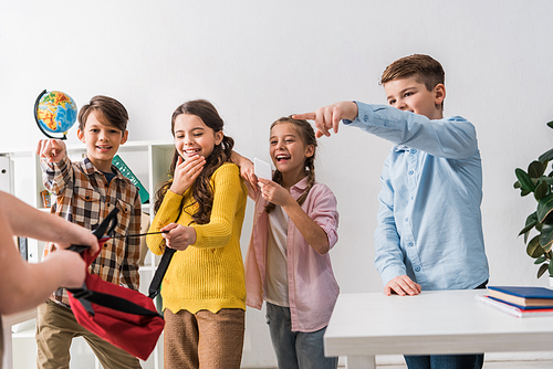 selective focus of cruel schoolkids pointing with fingers at bullied classmate