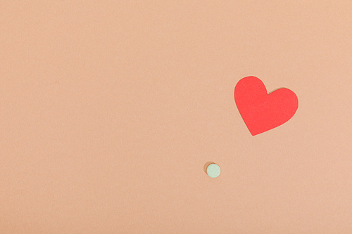 Top view of paper heart and pill on brown surface