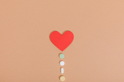 Top view of paper heart and pills on brown surface