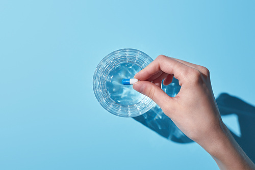 cropped view of woman putting pill in glass with water on blue background