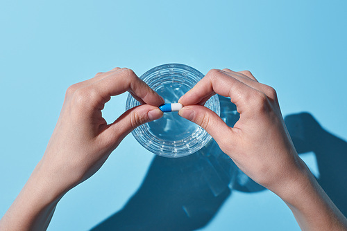 partial view of woman putting pill in glass with water on blue background