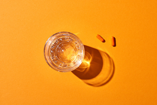 top view of pills near glass with water on orange background