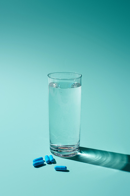 transparent glass with fresh water and blue pills on turquoise background