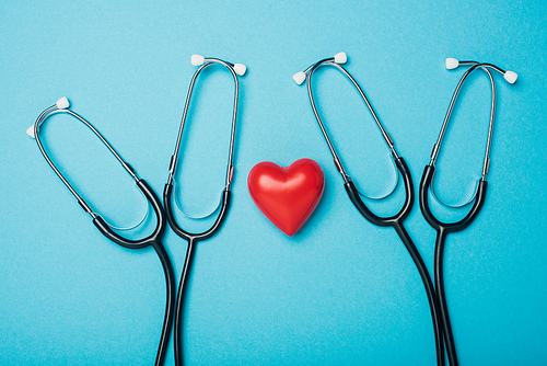 Top view of decorative red heart with stethoscopes on blue background, world health day concept