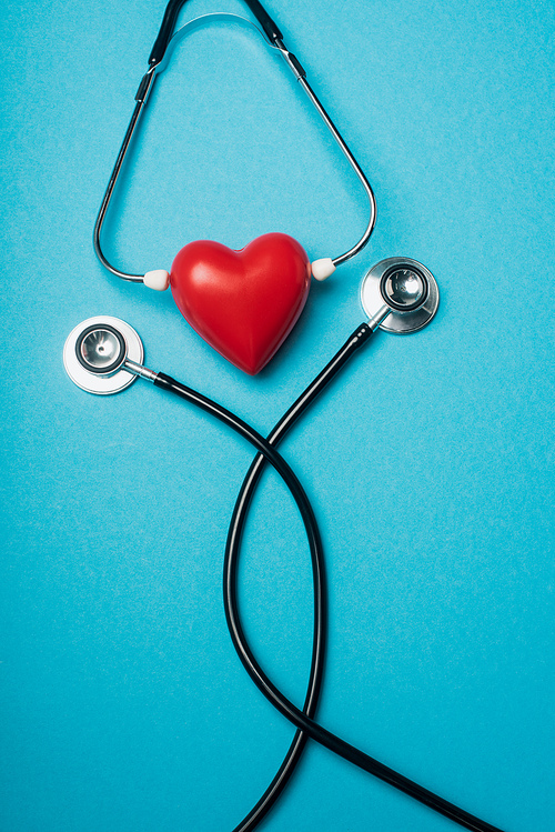 Top view of decorative red heart with black stethoscope on blue background, world health day concept