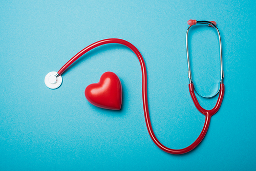 Top view of decorative heart next to red stethoscope on blue background, world health day concept