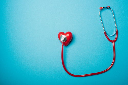 Top view of decorative heart connected with red stethoscope on blue background, world health day concept