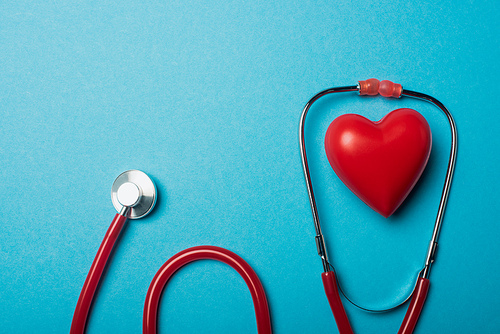 Top view of red heart and stethoscope on blue background, world health day concept