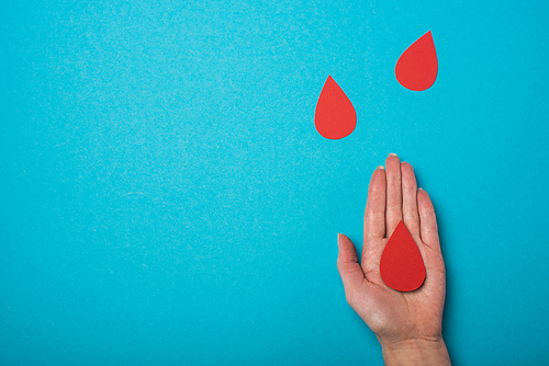 Top view of woman palm with decorative drops of blood on blue background, world health day concept