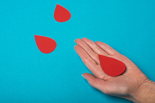 Cropped view of woman palm with decorative drops of blood on blue background, world health day concept