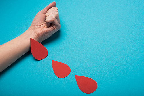 Cropped view of imitation of drops of blood from woman hand on blue background, world health day concept