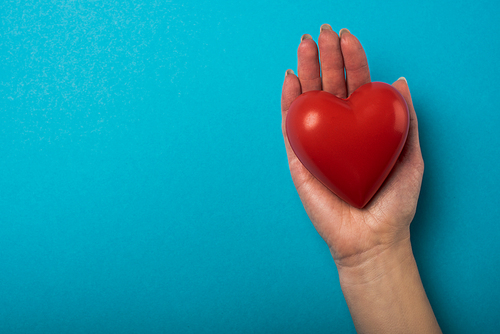 Top view of woman holding decorative red heart on blue background, world health day concept