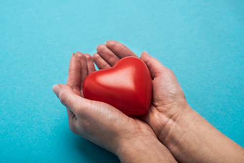 Cropped view of decorative red heart in woman hands on blue background, world health day concept