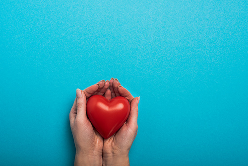 Top view of decorative red heart in woman hands on blue background, world health day concept