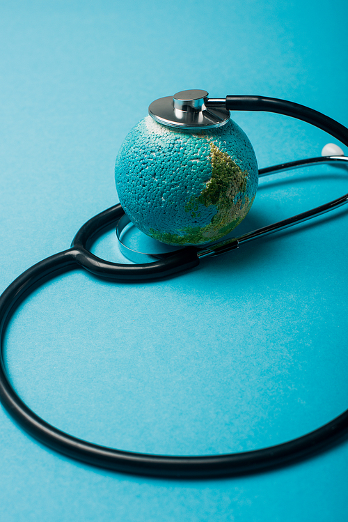 Black stethoscope connected with globe on blue background, world health day concept