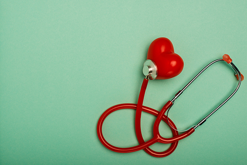 Top view of red stethoscope connected with decorative heart on green background, world health day concept