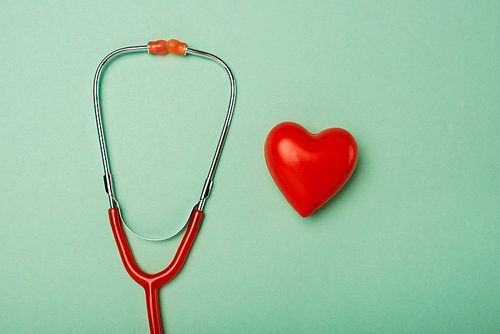 Top view of red stethoscope with decorative heart on green background, world health day concept