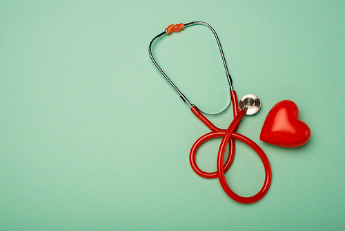 Top view of stethoscope next to red heart on green background, world health day concept