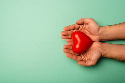 Top view of man holding decorative red heart on green background, world health day concept