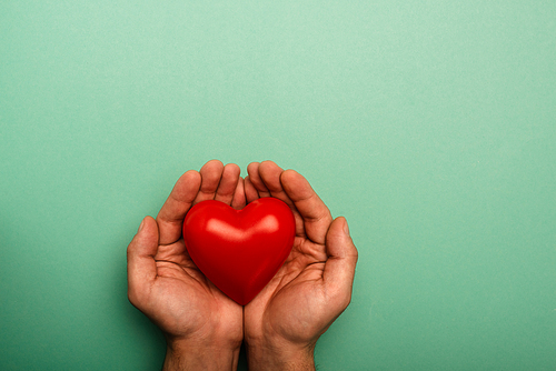 Top view of decorative red heart in man hands on green background, world health day concept