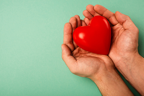 Cropped view of decorative red heart in man hands on green background, world health day concept