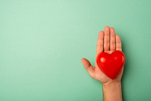 Top view of decorative red heart in man hand on green background, world health day concept