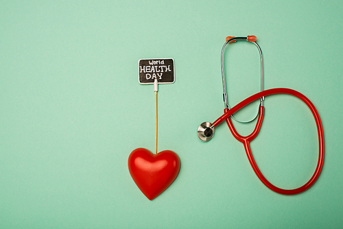 Top view of stethoscope, decorative heart and card with world health day lettering on green background