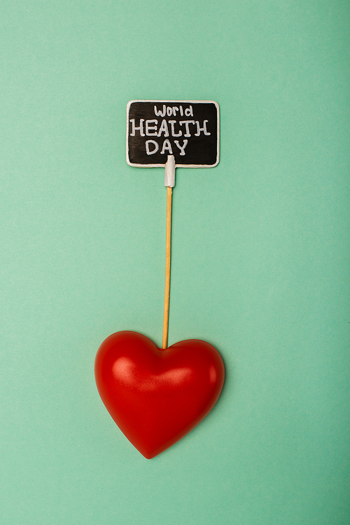 Top view of decorative red heart and card with world health day lettering on green background