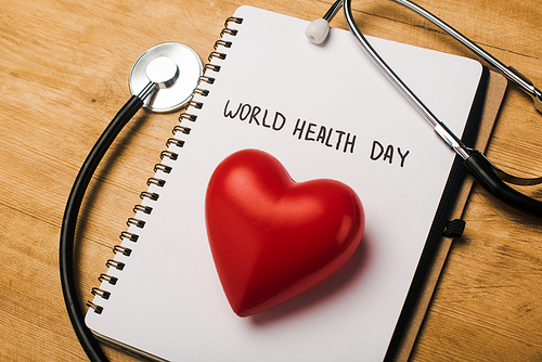 Stethoscope, decorative red heart on notebook with world health day lettering on wooden background