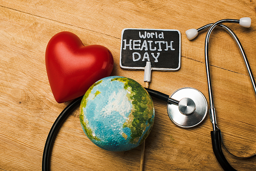 Top view of decorative red heart, stethoscope, globe and card with world health day lettering on wooden background