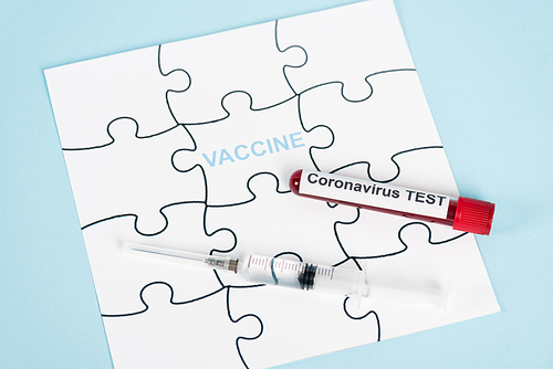 puzzle pieces with vaccine lettering near sample with coronavirus test and syringe on blue