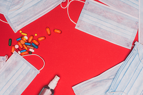 Top view of hand sanitizer near pills and medical masks on red background