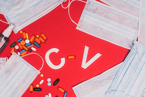 Top view of hand sanitizer, pills with medical masks and cv letters on red background