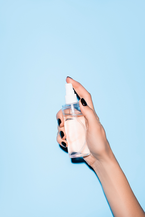 cropped view of woman holding hand sanitizer on blue