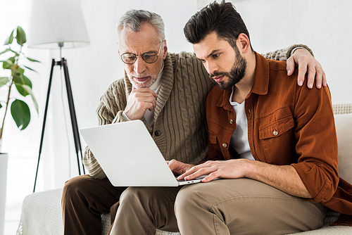 handsome man sitting with senior father and looking at laptop